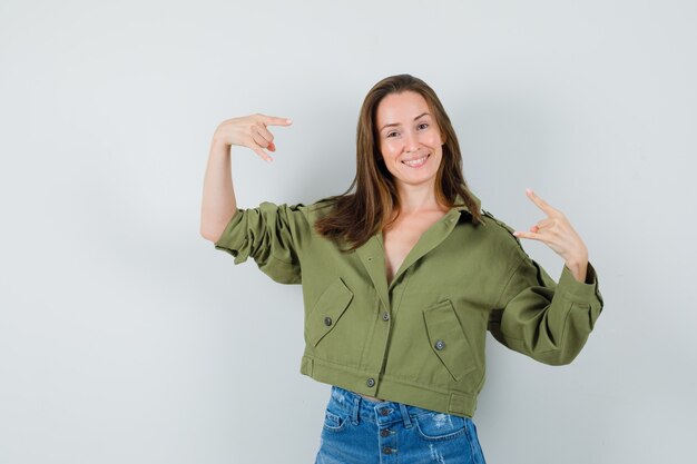 Señorita haciendo símbolo de rock en pantalones cortos de chaqueta verde y mirando confiado