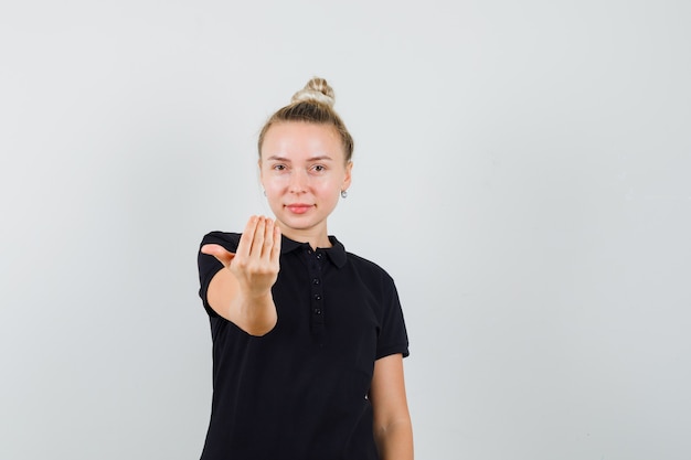 Señorita invitando a venir en camiseta negra y luciendo confiada