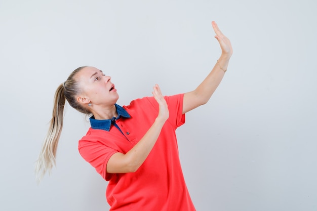 Señorita levantando las manos de manera preventiva en camiseta y mirando asustada