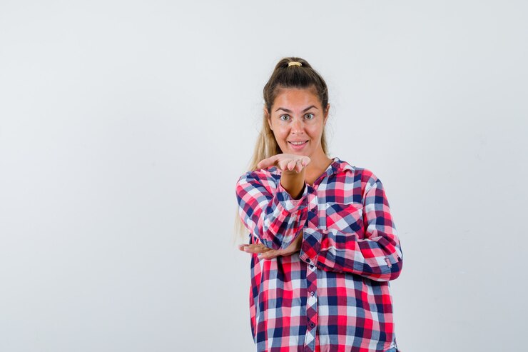 Foto gratuito señorita manteniendo la mano extendida en camisa a cuadros y mirando alegre, vista frontal.