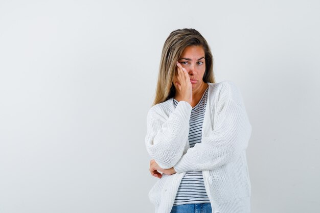 Señorita manteniendo la mano en la mejilla en camiseta, chaqueta y con aspecto cansado. vista frontal.