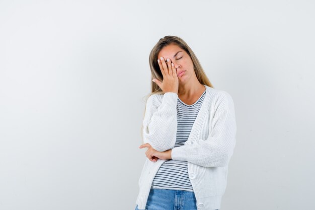 Señorita manteniendo la mano en el ojo en camiseta, chaqueta y con aspecto cansado. vista frontal.