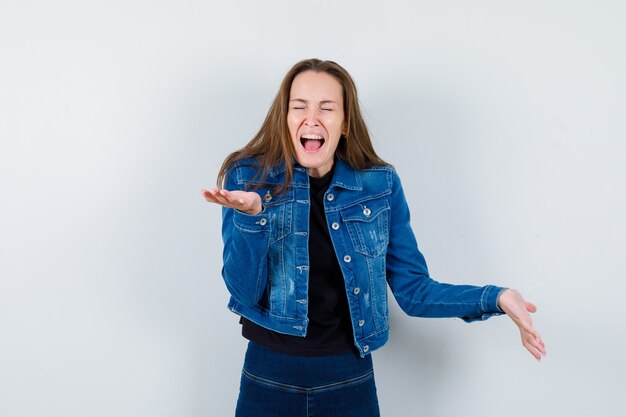 Señorita manteniendo las manos en gesto de interrogación mientras grita en blusa, chaqueta y parece agitada, vista frontal.