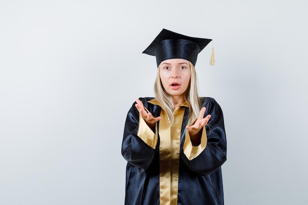 Señorita manteniendo las manos de manera agresiva en traje académico y mirando molesto.