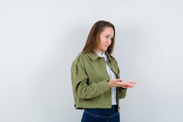 Señorita manteniendo las palmas abiertas en camisa, chaqueta y luciendo delicada, vista frontal.