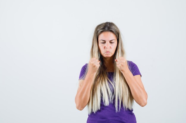 Señorita manteniendo los puños apretados en camiseta violeta y luciendo fuerte. vista frontal.