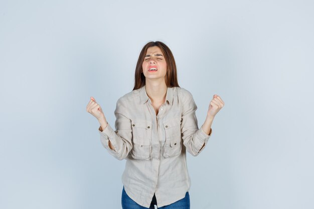 Señorita manteniendo los puños apretados, cerrando los ojos en casual, jeans y luciendo frustrada. vista frontal.