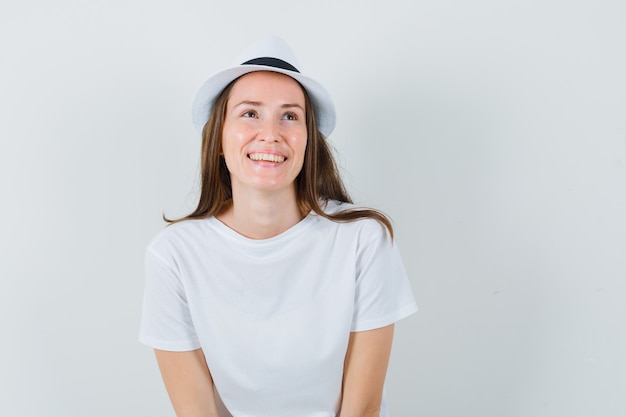 Señorita mirando hacia arriba con sombrero de camiseta blanca y mirando alegre