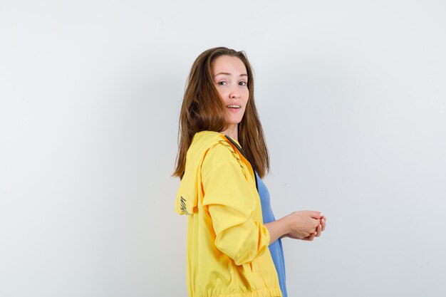 Señorita mirando a la cámara con las manos entrelazadas en camiseta, chaqueta y mirando confiado.