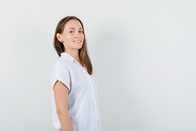 Señorita mirando a un lado mientras sonríe en blusa blanca y parece contenta.