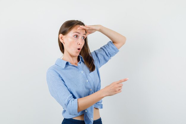 Señorita mirando lejos mientras apunta al lado con camisa azul, pantalones y mirando sorprendido