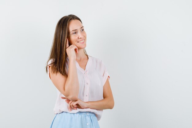 Señorita mirando a otro lado mientras piensa en camiseta, falda y parece optimista. vista frontal.