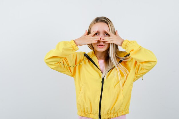 Señorita mirando a través de los dedos en camiseta, chaqueta y buscando pacífica