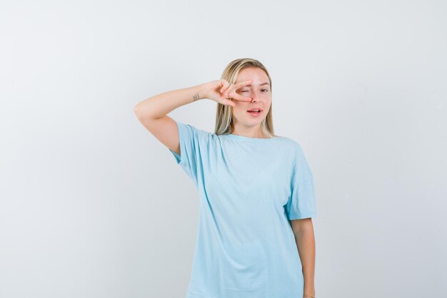 Señorita mirando a través de los dedos en camiseta y mirando feliz aislado