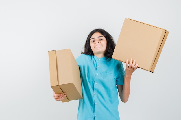 Señorita mostrando cajas en camisa azul y mirando confundida.