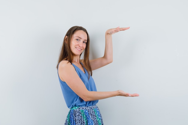 Foto gratuita señorita mostrando cartel de gran tamaño en blusa azul, falda y mirando contento, vista frontal.