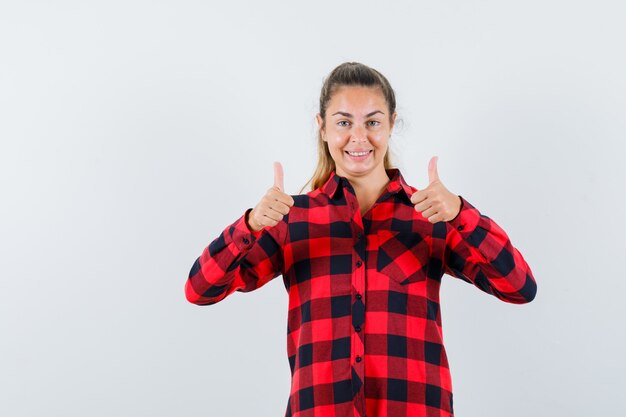 Señorita mostrando doble pulgar hacia arriba en camisa a cuadros y mirando feliz