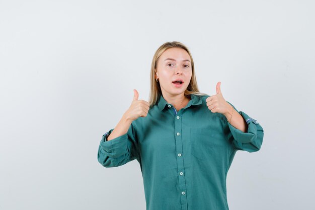 Señorita mostrando doble pulgar hacia arriba en camisa verde y mirando feliz