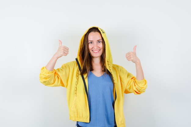 Señorita mostrando doble pulgar hacia arriba en camiseta, chaqueta y mirando feliz. vista frontal.