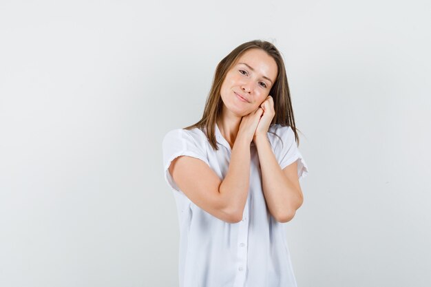 Señorita mostrando gesto de almohada en blusa blanca y mirando tranquilo