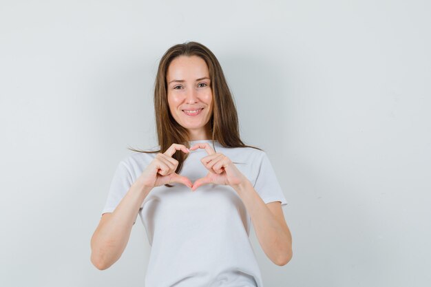 Señorita mostrando gesto de corazón en camiseta blanca y mirando alegre