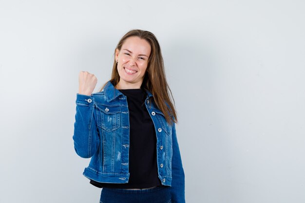 Señorita mostrando gesto ganador en blusa, chaqueta y mirando confiado, vista frontal.