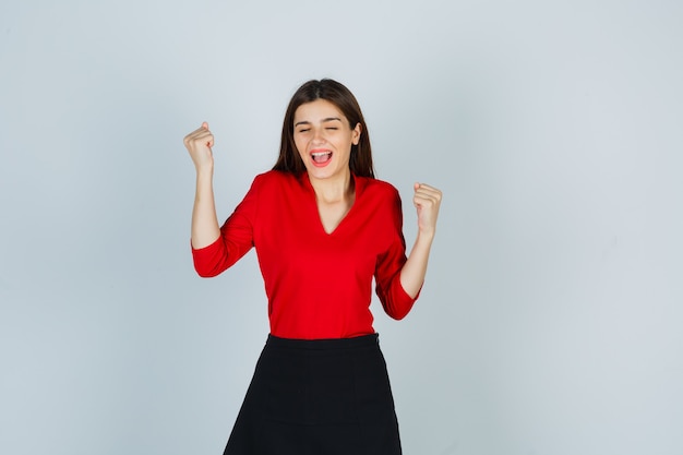 Señorita mostrando gesto de ganador en blusa roja, falda negra y con suerte