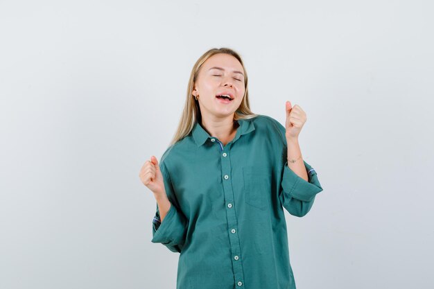 Señorita mostrando gesto de ganador en camisa verde y mirando feliz