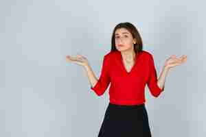 Foto gratuita señorita mostrando gesto de impotencia en blusa roja, falda y mirando estresado