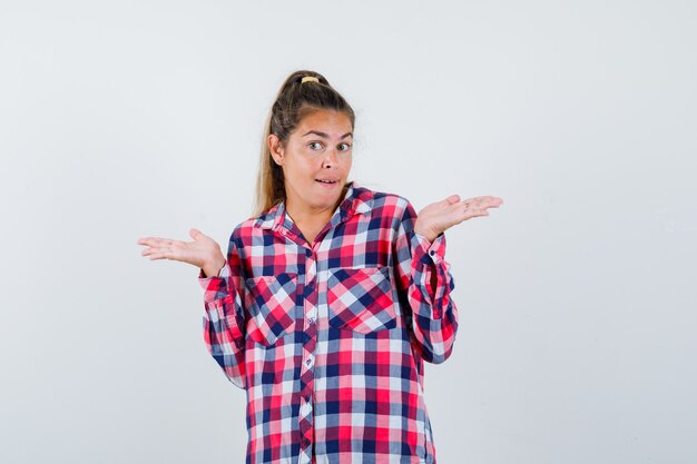 Señorita mostrando gesto de impotencia en camisa a cuadros y mirando confundido. vista frontal.