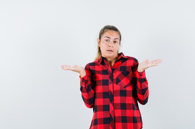 Señorita mostrando gesto de impotencia en camisa a cuadros y mirando confundido