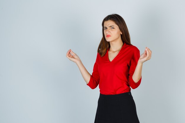 Señorita mostrando gesto de meditación en blusa roja, falda y buscando pacífica