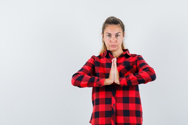 Señorita mostrando gesto de namaste en camisa a cuadros y mirando confiado