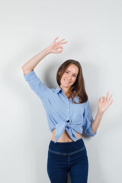 Señorita mostrando gesto ok en camisa azul, pantalones y mirando complacido