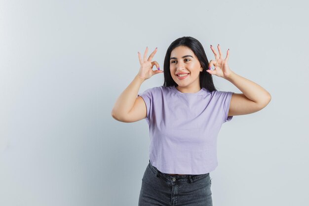 Señorita mostrando gesto ok en camiseta, jeans y mirando feliz. vista frontal.