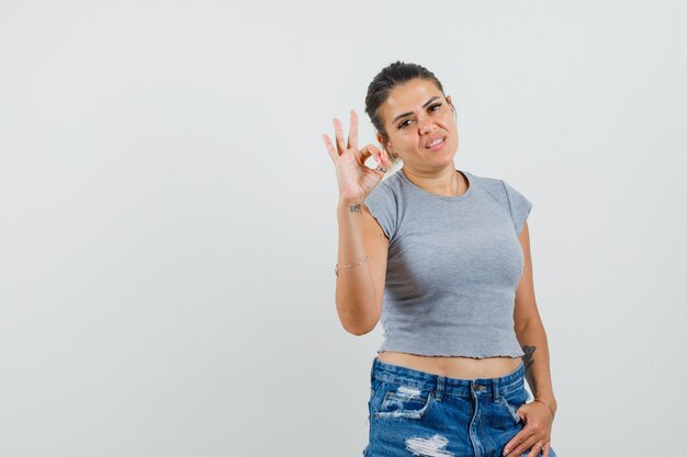 Señorita mostrando gesto ok en camiseta, pantalones cortos y mirando confiado