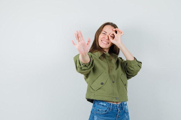 Foto gratuita señorita mostrando gesto de parada con signo de ok en el ojo en pantalones cortos de chaqueta verde