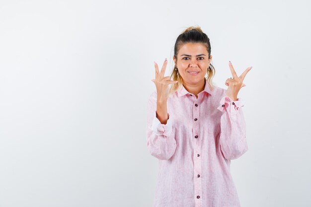 Señorita mostrando gesto de paz en camisa rosa y mirando feliz