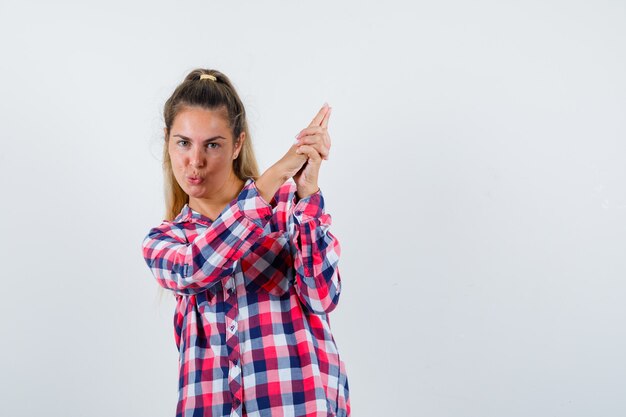 Señorita mostrando gesto de pistola en camisa a cuadros y mirando confiado. vista frontal.