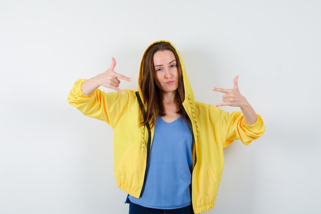 Señorita mostrando gesto de rock en camiseta, chaqueta y mirando confiado, vista frontal.