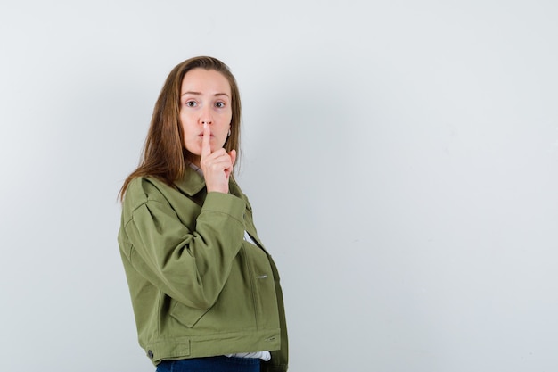 Señorita mostrando gesto de silencio en camisa, chaqueta y mirando con cuidado, vista frontal.