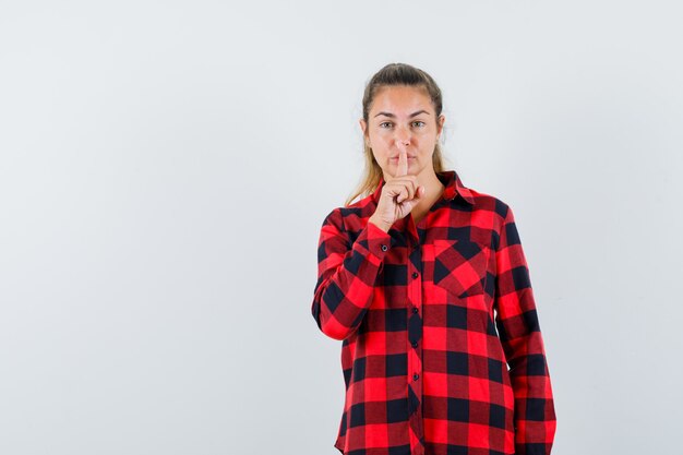 Señorita mostrando gesto de silencio en camisa a cuadros y mirando confiado