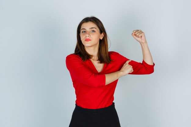 Señorita mostrando los músculos del brazo en blusa roja, falda y mirando confiado