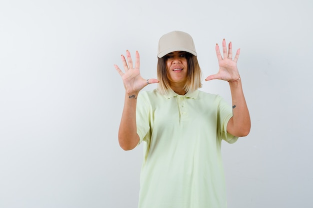 Señorita mostrando palmas en gesto de rendición en camiseta, gorra y mirando indefenso, vista frontal.