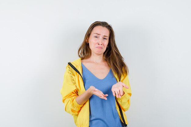 Señorita mostrando palmas vacías en camiseta, chaqueta y mirando angustiado, vista frontal.