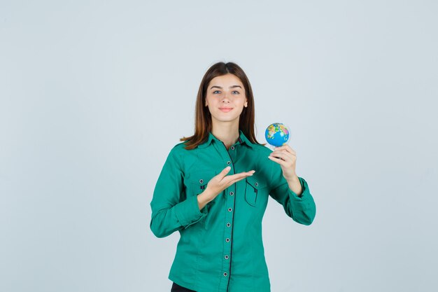 Señorita mostrando un pequeño globo terráqueo en camisa y mirando complacido, vista frontal.