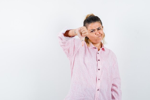 Señorita mostrando el pulgar hacia abajo en camisa rosa y mirando descontento