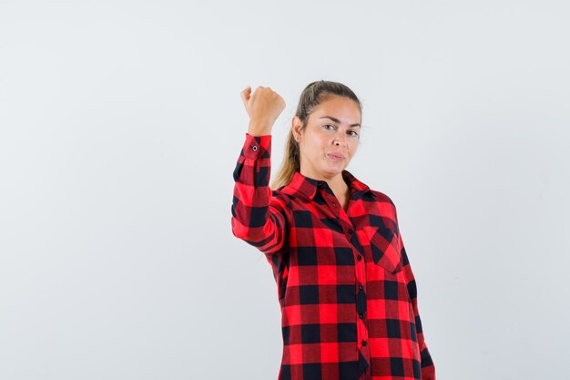 Señorita mostrando el puño cerrado en camisa a cuadros y mirando confiado