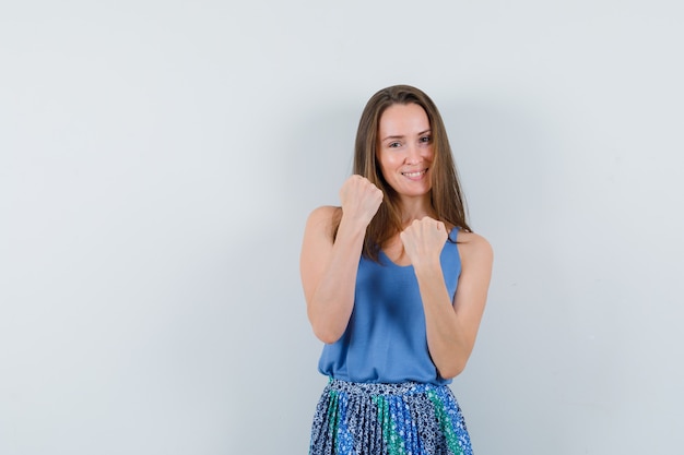 Señorita mostrando puños cerrados en camiseta, falda y mirando confiado