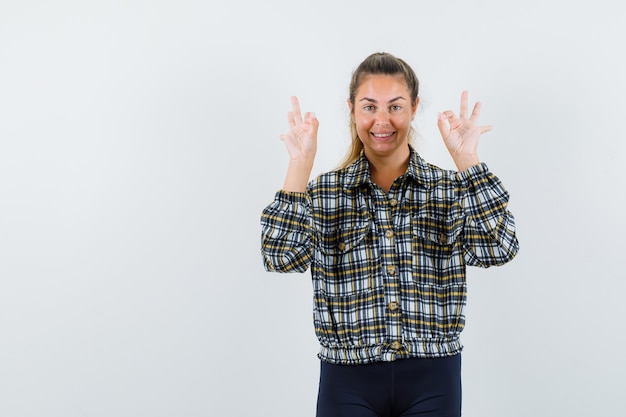 Señorita mostrando signo ok en camisa, pantalones cortos y con aspecto optimista. vista frontal.